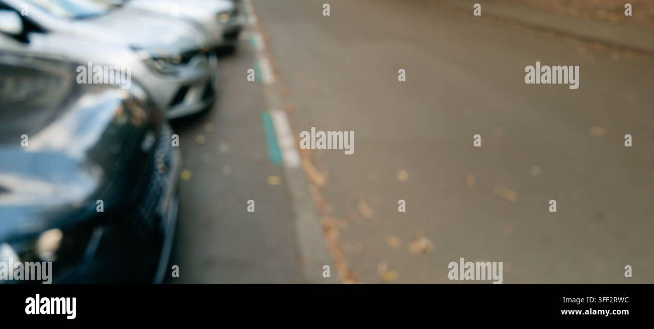 Auto parcheggiate sfocate allineano una strada con spazio libero sulla strada. L'immagine si adatta alla pubblicità per il parcheggio, il trasporto, la mobilità e lo sfondo urbano Foto Stock