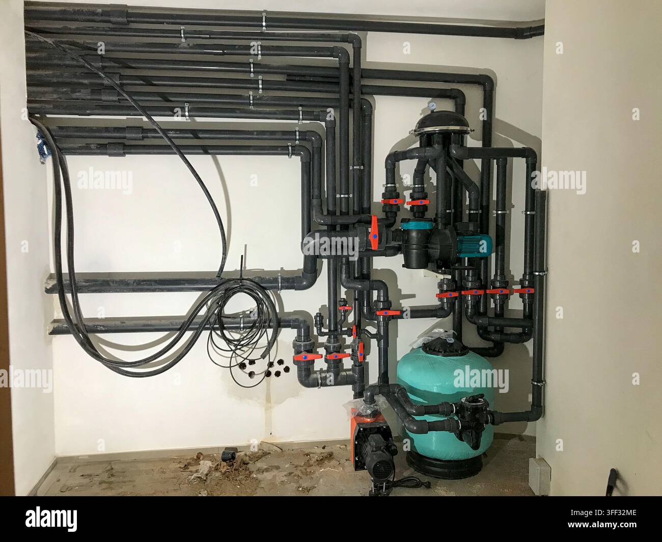 Sistema di filtraggio dell'acqua della piscina con una serie di tubi in pvc nero, valvole, pompe e un filtro di sabbia installato su una parete bianca in un roo meccanico Foto Stock