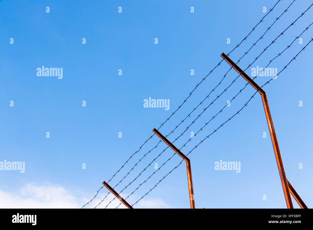 Pali di recinto di filo spinato in carcere contro un cielo blu Foto Stock