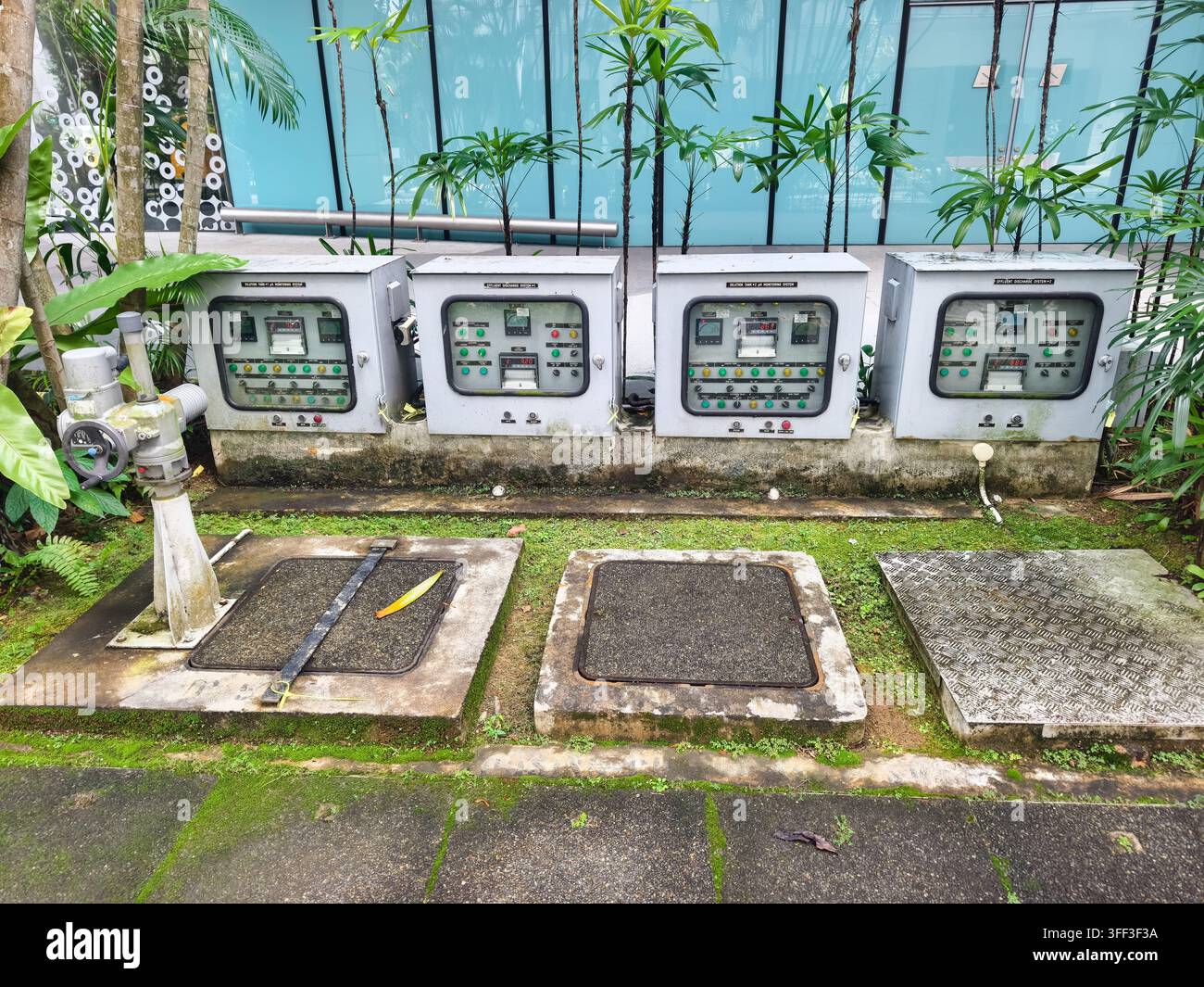 Pannelli di controllo elettrici esterni su una base in cemento, botole di accesso sotterranee per le utenze e un sistema di valvole di controllo dell'acqua automatizzato. Singapore Foto Stock