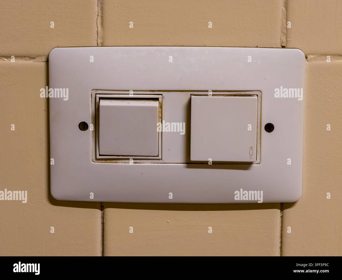 Pannello elettrico rettangolare bianco con interruttore luce e pulsante campanello, che mostra segni di usura e sporcizia, fissato su una parete piastrellata gialla in alm Foto Stock