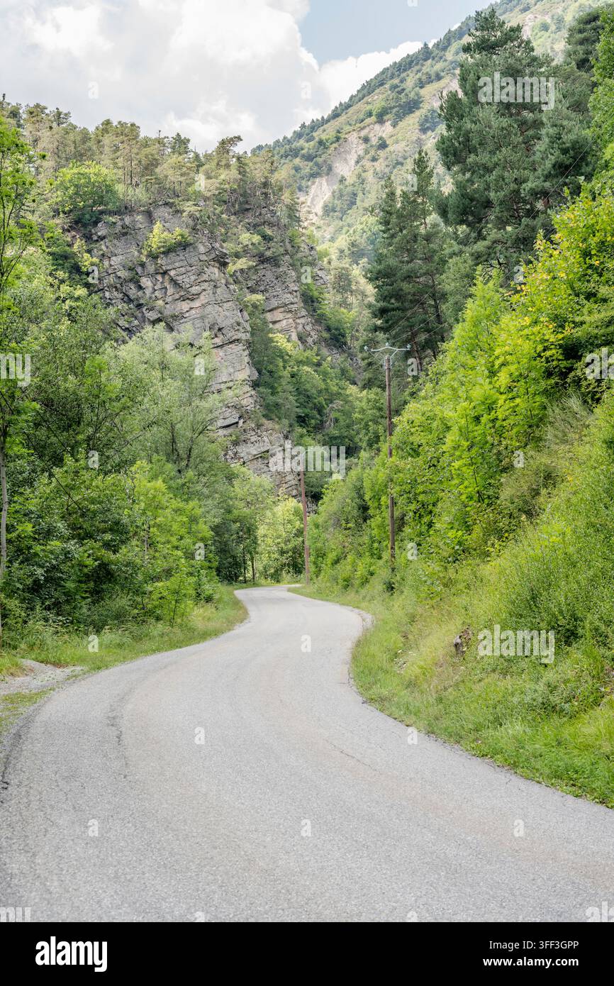 Paesaggio con strada tortuosa D900 sotto scogliere rocciose verticali a strapiombo nella valle del fiume Le Bes, ripreso sotto una luce estiva brillante nella gola di Vedaches Clue, P Foto Stock