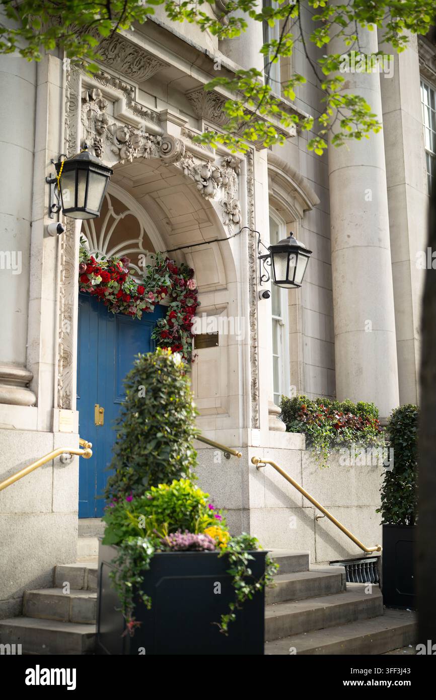 Esposizioni floreali rosse adornano l'ingresso blu del vecchio municipio di Chelsea su King's Road, Londra, stilizzato per matrimoni. Foto Stock