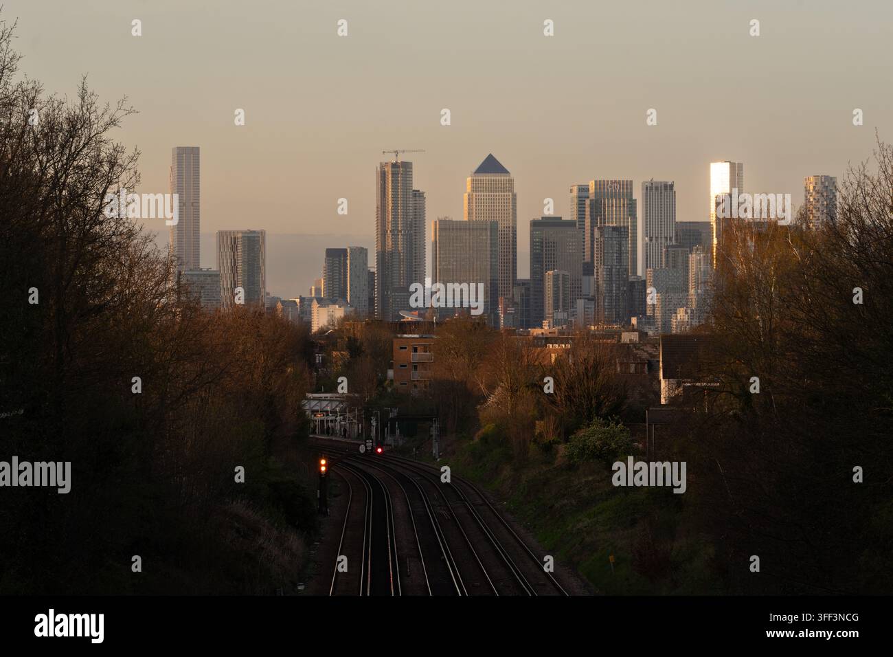 La luce dell'ora dorata si riflette sullo skyline di Canary Wharf a Londra (One Canada Square) dai binari ferroviari vicino alla stazione di Canary Wharf. Foto Stock