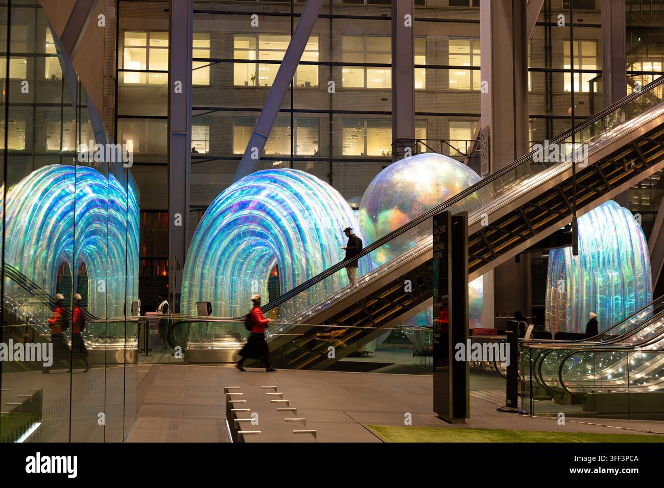 I pedoni percorrono le scale mobili del Leadenhall Building di Londra, passando accanto a installazioni artistiche iridescenti luminose durante il loro tragitto. Foto Stock