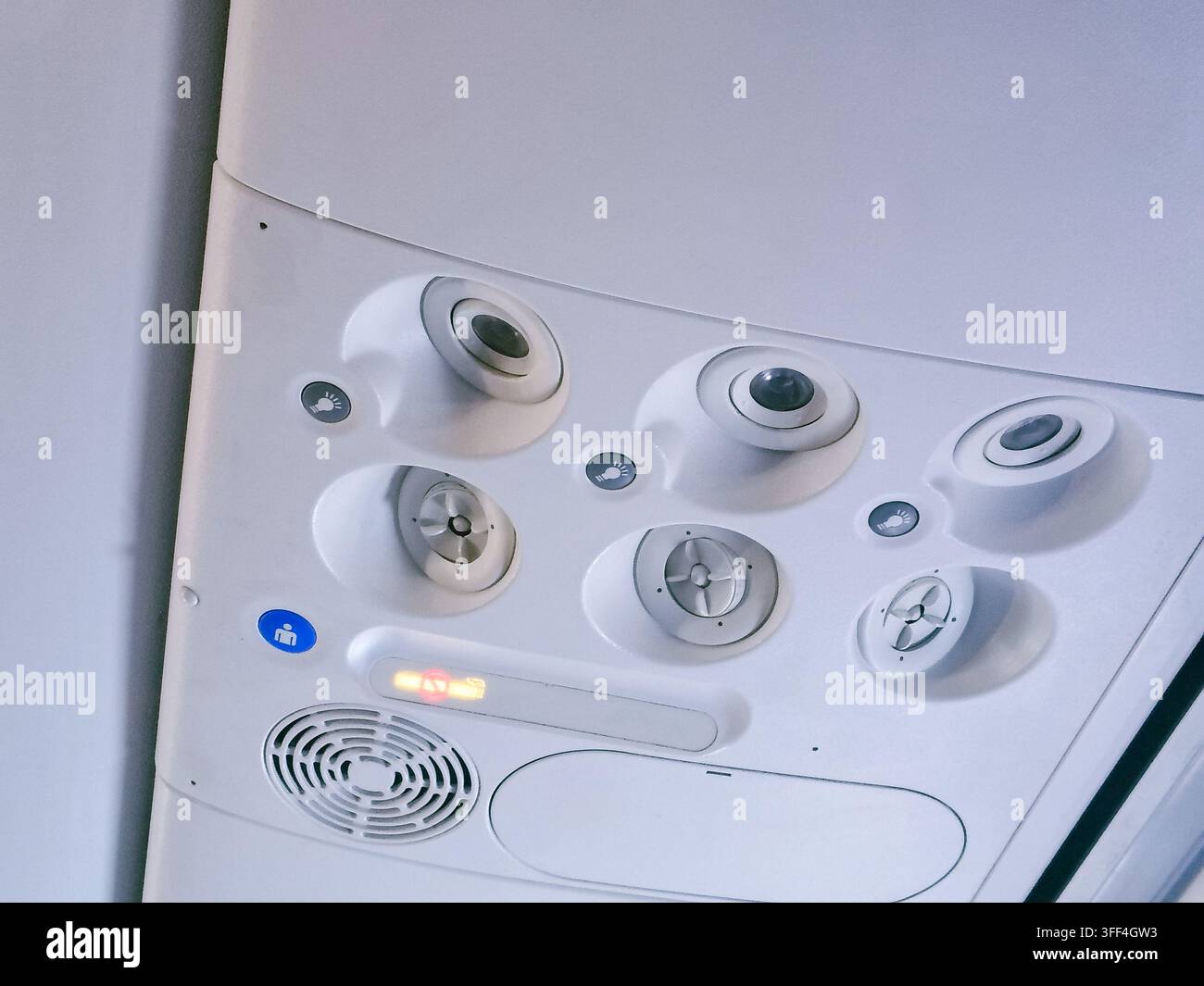 Primo piano del pannello sopraelevato passeggeri di un aereo di linea commerciale con prese d'aria regolabili, luci per leggere e segnali di avvertimento illuminati. Foto Stock