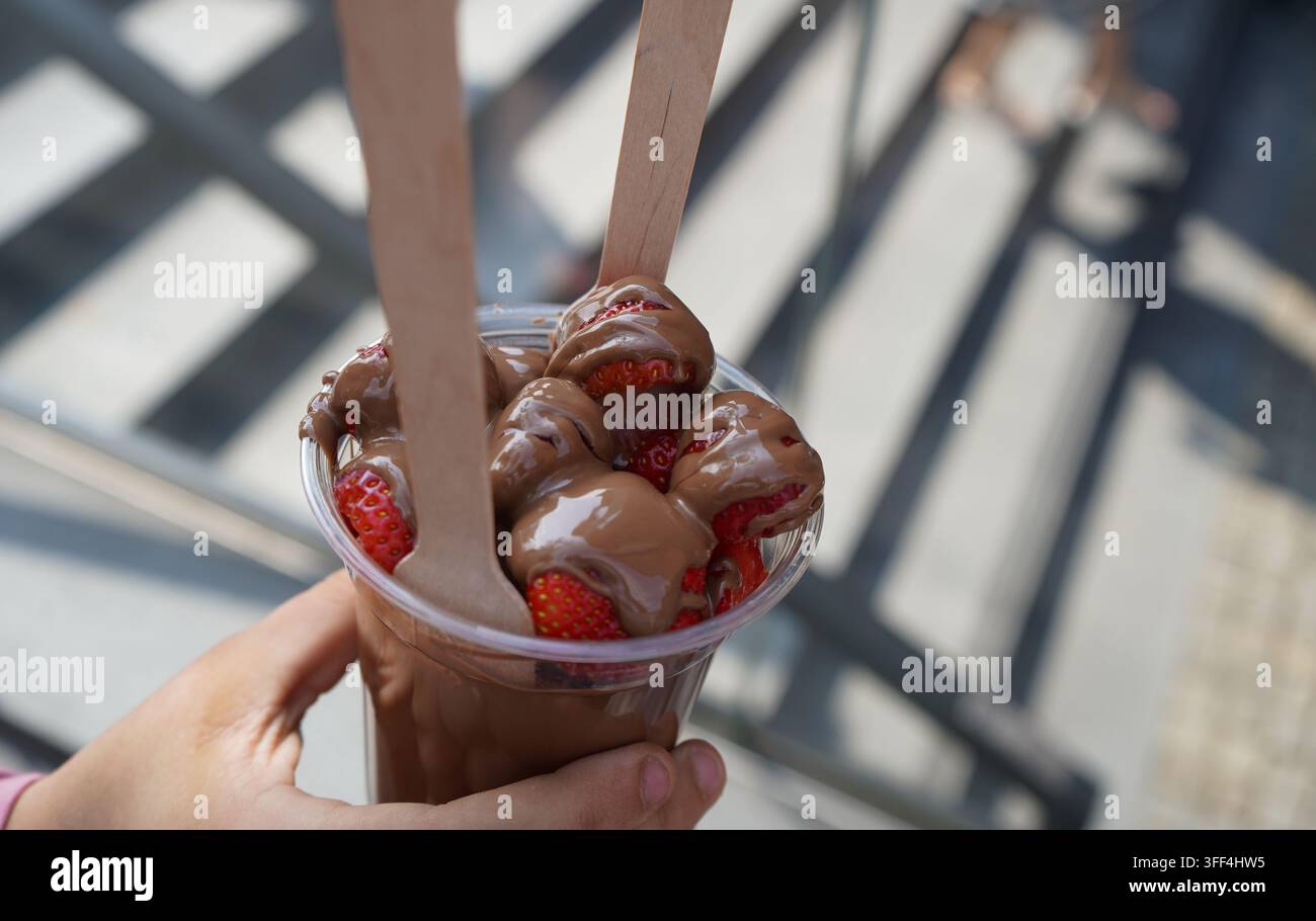 Prima di fresche fragole glassate con cioccolato fuso in una tazza con forchette di legno. Foto Stock