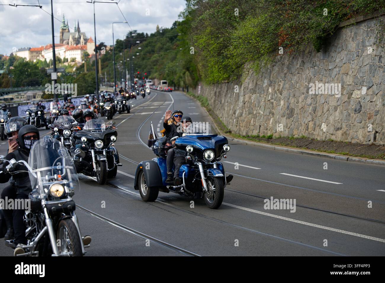 Un passeggero saluta da una moto blu a tre ruote durante la parata dei Prague Harley Days 2026 sotto il castello di Praga. Foto Stock