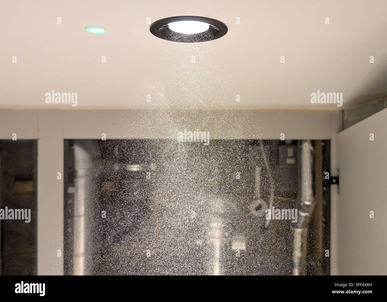 Particelle di polvere fine sospesa illuminate da una luce a soffitto all'interno di un'area di costruzione e servizi edilizi, che illustra la polvere da costruzione Foto Stock