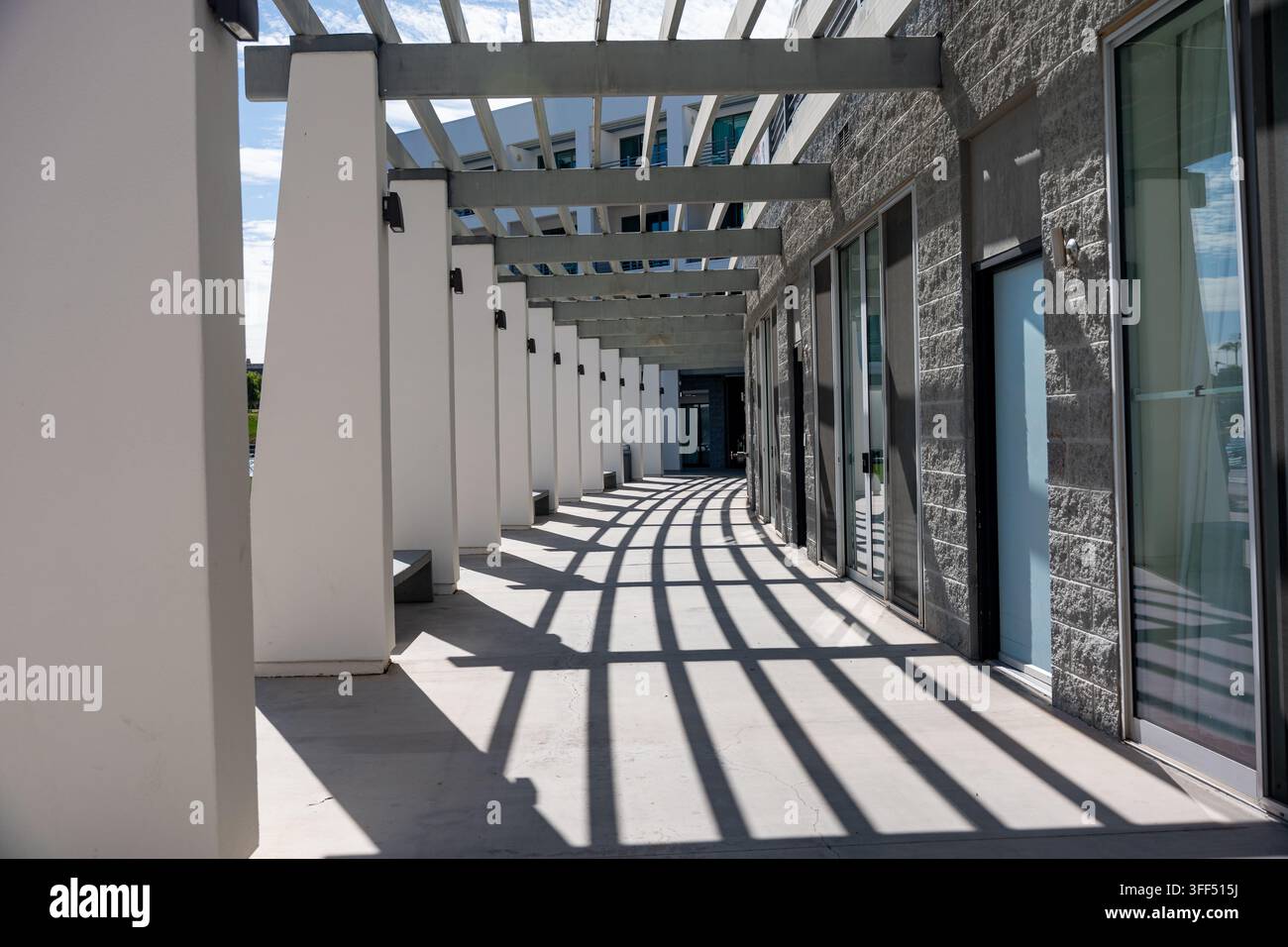 Un moderno passaggio pedonale all'aperto presenta colonne ripetitive, travi sopra la testa, porte di vetro e ombre geometriche drammatiche Foto Stock