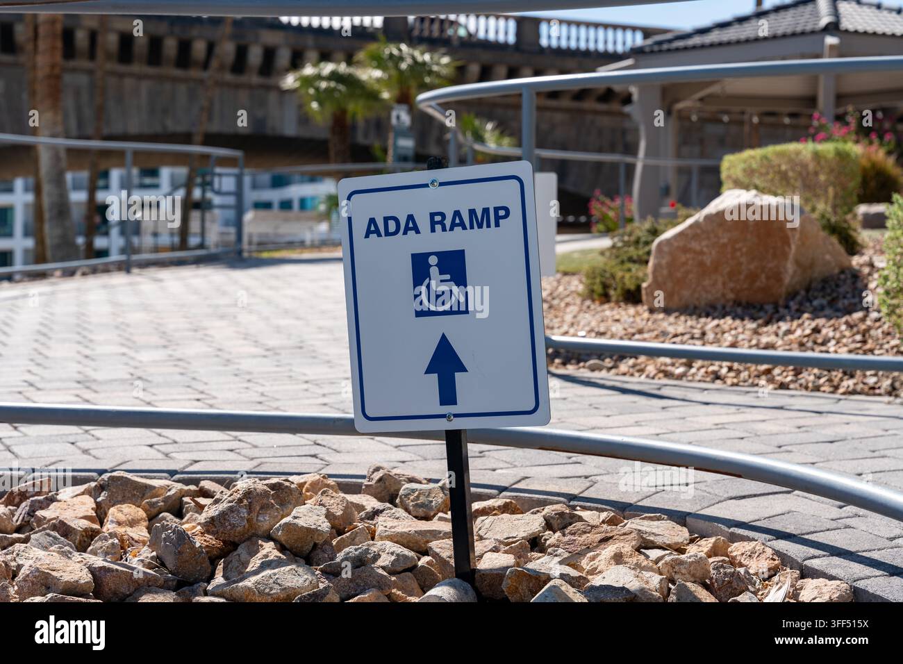 Vista ravvicinata di un cartello di rampa ADA con il Simbolo Internazionale di Accessibilità e una freccia direzionale accanto a un marciapiede pavimentato accessibile. Foto Stock