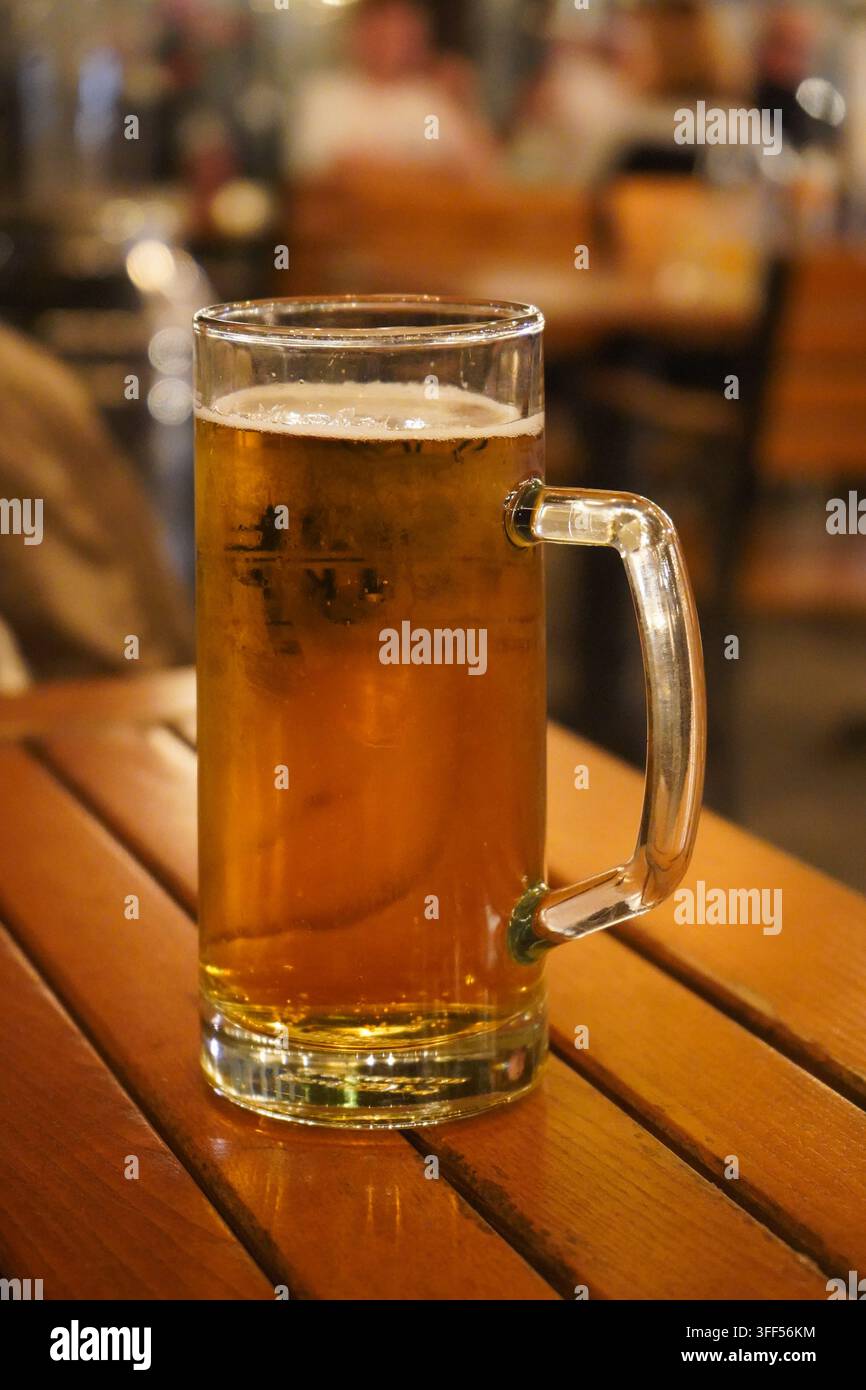Bicchiere di vetro pieno di birra alla spina fredda con schiuma bianca posato su un tavolo di legno in un bar all'aperto di notte. Foto Stock