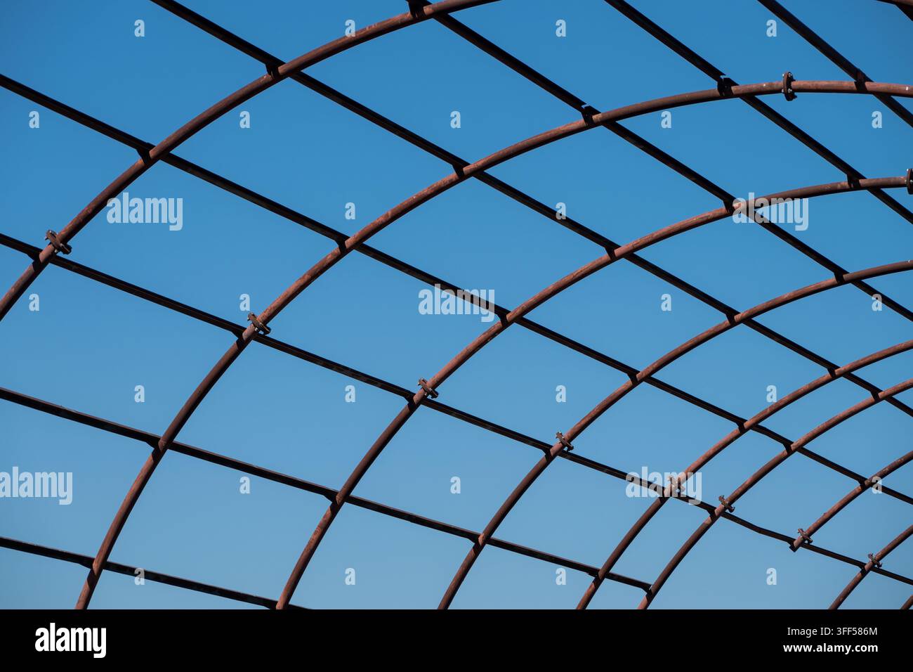 un primo piano, vista astratta di una struttura a griglia metallica curva e arrugginita che si interseca contro un cielo blu chiaro e solido Foto Stock