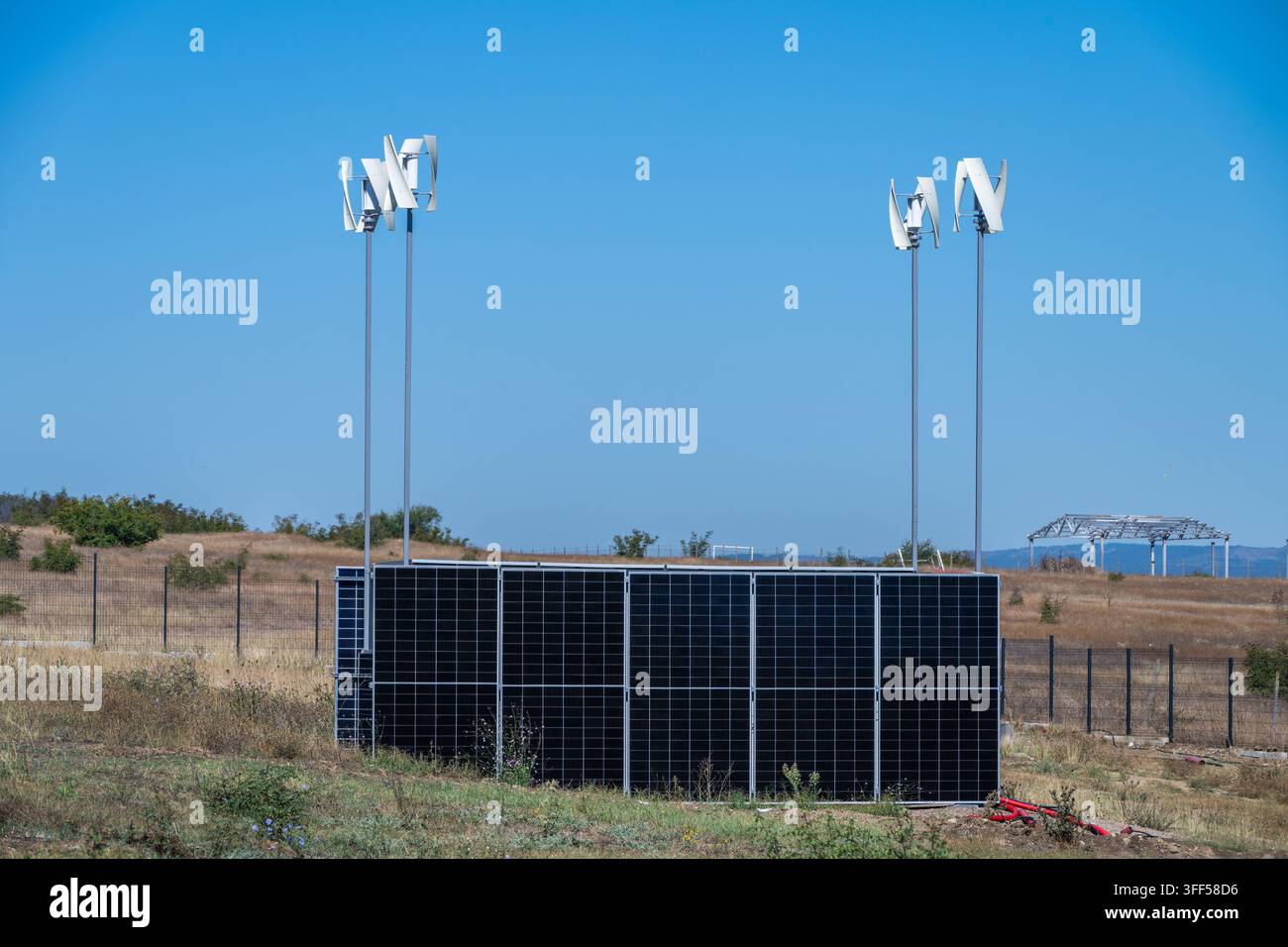 un sistema ibrido di energia rinnovabile off-grid che combina un array di pannelli solari scuri con quattro turbine eoliche verticali bianche in un campo rurale arido sotto un Foto Stock
