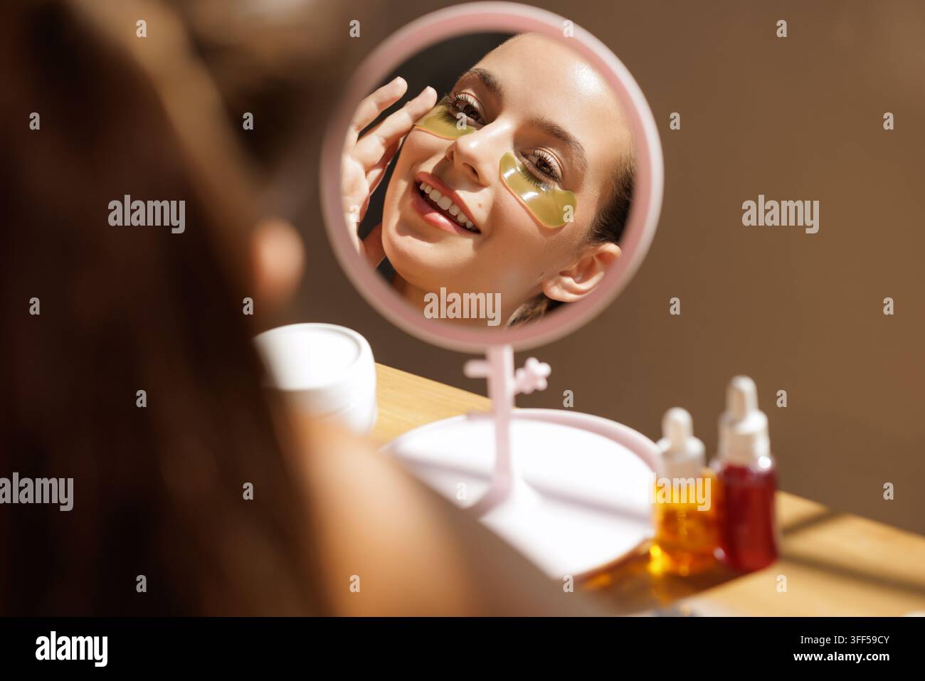 Una donna che utilizza patch occhi coreani per ridurre gonfiore e occhiaie, migliorando la sua routine di cura della pelle a casa. Foto Stock