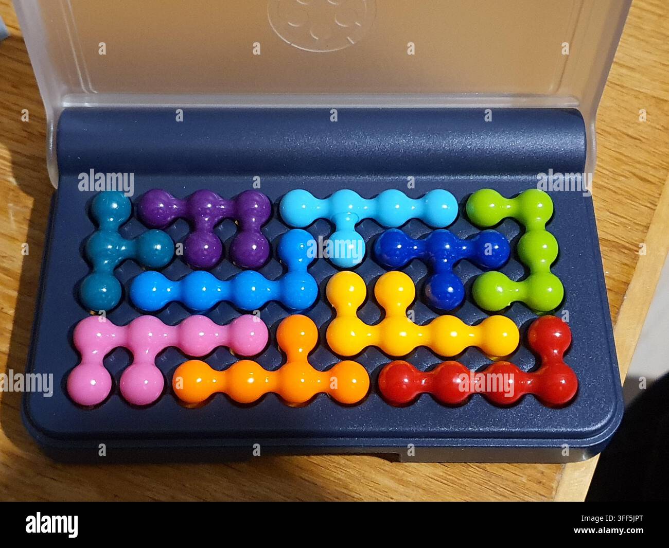 Una vista ravvicinata di un gioco di puzzle logico 3D colorato disposto all'interno di una scatola di plastica blu scuro aperta con coperchio trasparente. Il puzzle è composto da nove Foto Stock