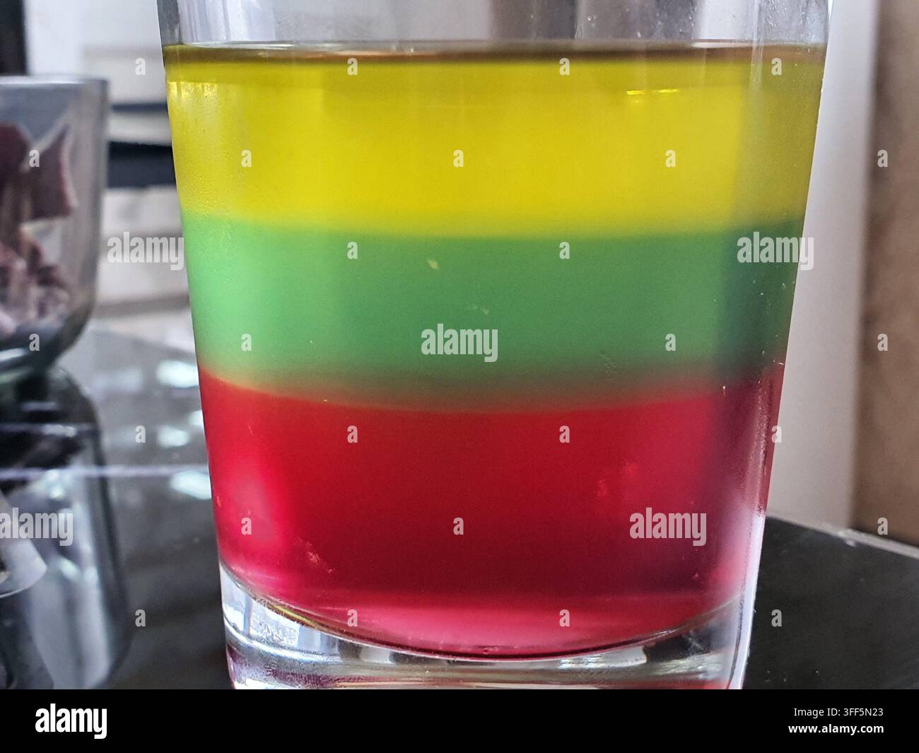 Una fotografia ravvicinata di un bicchiere trasparente contenente tre strati orizzontali distinti di liquido colorato, che dimostra differenze di densità e liquido Foto Stock