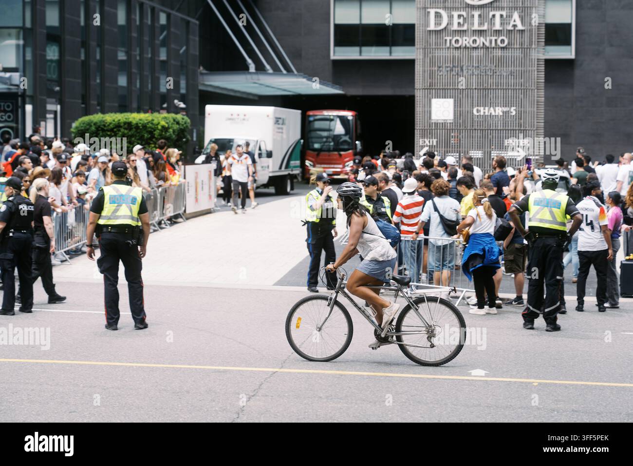 Toronto, Canada - 20 giugno 2026: Ciclista supera una folla e la polizia fuori dall'hotel Delta di Toronto Foto Stock