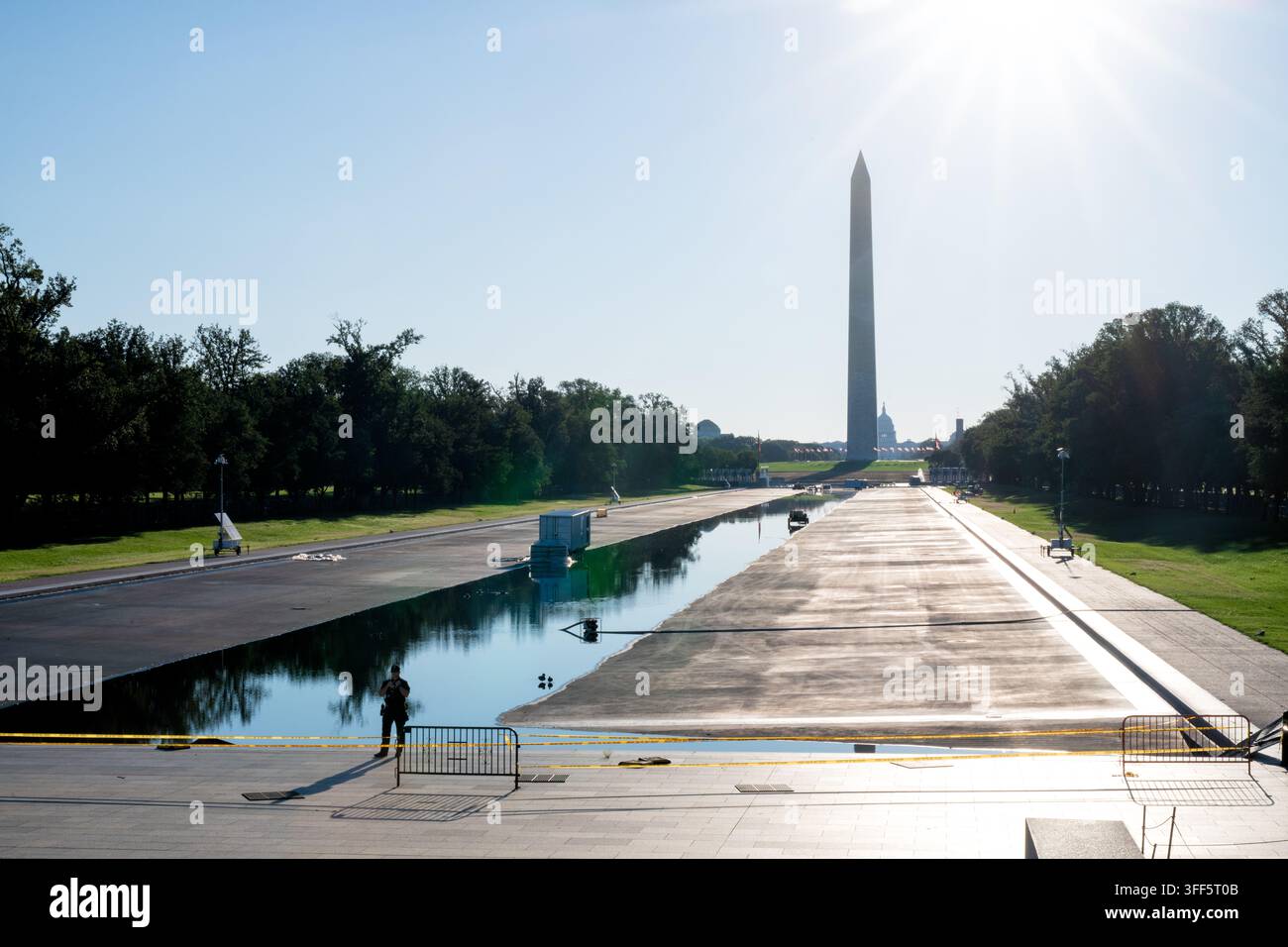 Riparazioni alla piscina riflettente vicino al Washington Monument e al Campidoglio | WASHINGTON, D.C. — Un agente di sicurezza si trova accanto alla piscina riflettente parzialmente svuotata del Lincoln Memorial sul National Mall, domenica 6 settembre 2026, con il Washington Monument e il Campidoglio degli Stati Uniti visibili in lontananza. Henry Bacon ha progettato la piscina, completata nel 1922-1923 come parte del Piano McMillan. Un progetto di risanamento avviato nell’aprile 2026 ha lasciato il bacino svuotato per mesi dopo che un rivestimento in poliurea è fallito e le alghe hanno contaminato l’acqua. I costi sono saliti oltre i 19 milioni di dollari tra tre appaltatori, con un quarto aggiunto alla fine di agosto Foto Stock