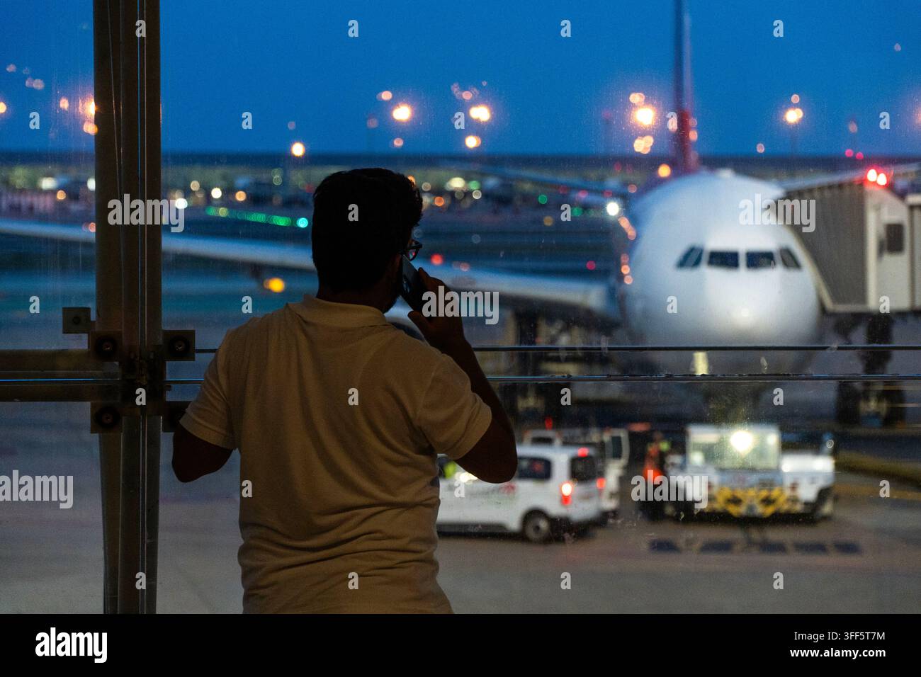 Una persona si trova a una finestra dell'aeroporto, osservando un grande aereo parcheggiato sulla pista. Foto Stock