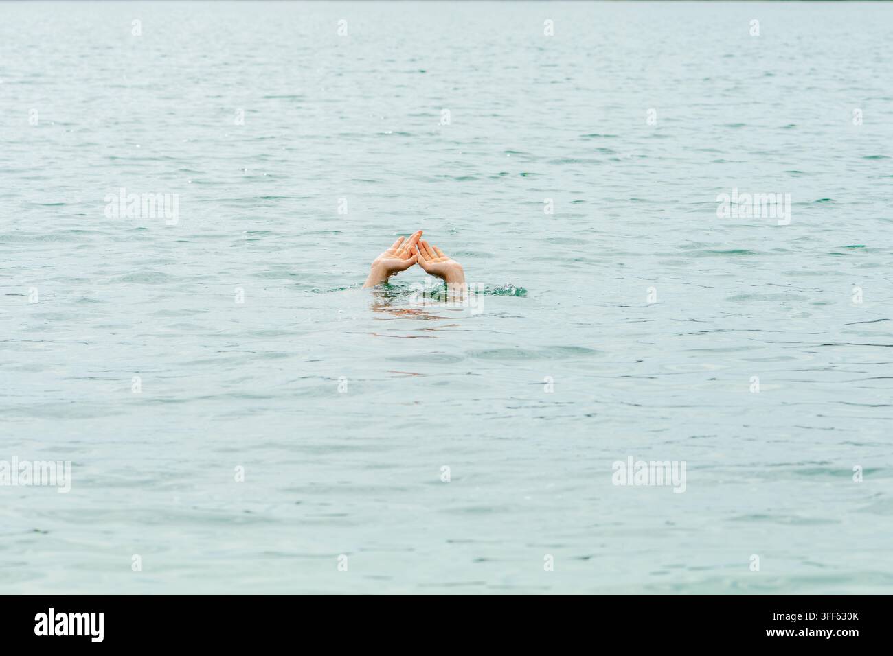 Due mani emergono da un'acqua calma, formando una piccola forma triangolare sopra la superficie. Foto Stock