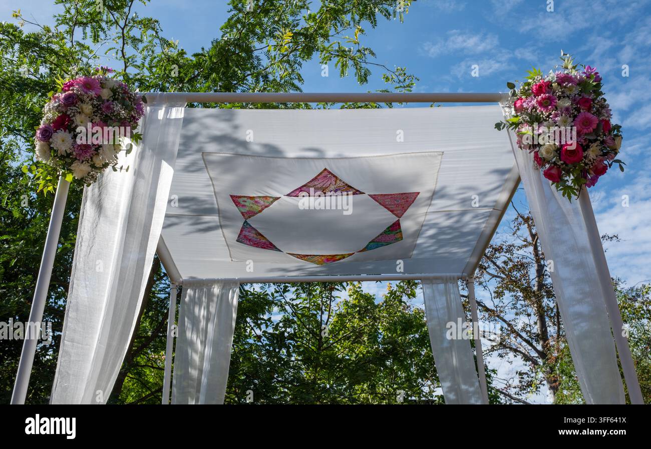 Tradizionale baldacchino nuziale Chuppah sotto il quale una coppia ebrea si sposa, in seta con un motivo a Stella di Davide. Decorato con fiori. Foto Stock