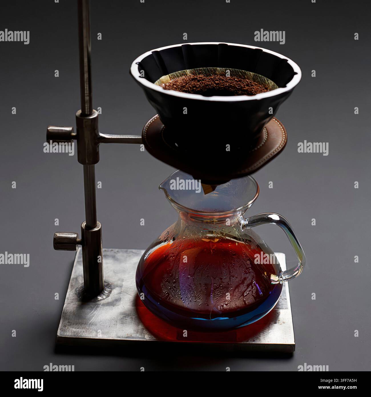Procedimento di preparazione del caffè con infusione a gravità con una caraffa di vetro e un supporto in metallo su uno sfondo scuro Foto Stock