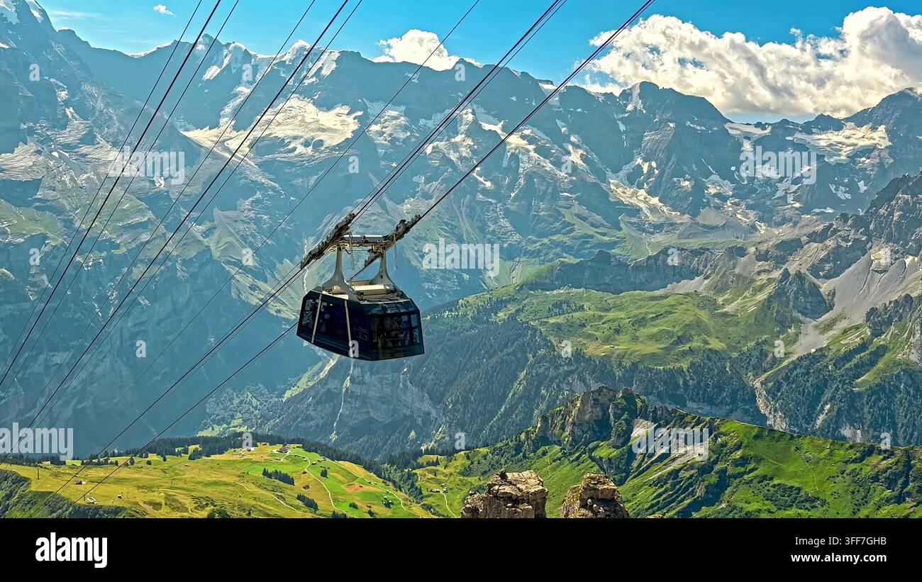Funivia sopra una valle alpina e cime innevate. La funivia attraversa una valle alpina verde sotto impervi picchi innevati, ghiacciai, rocciosi Foto Stock