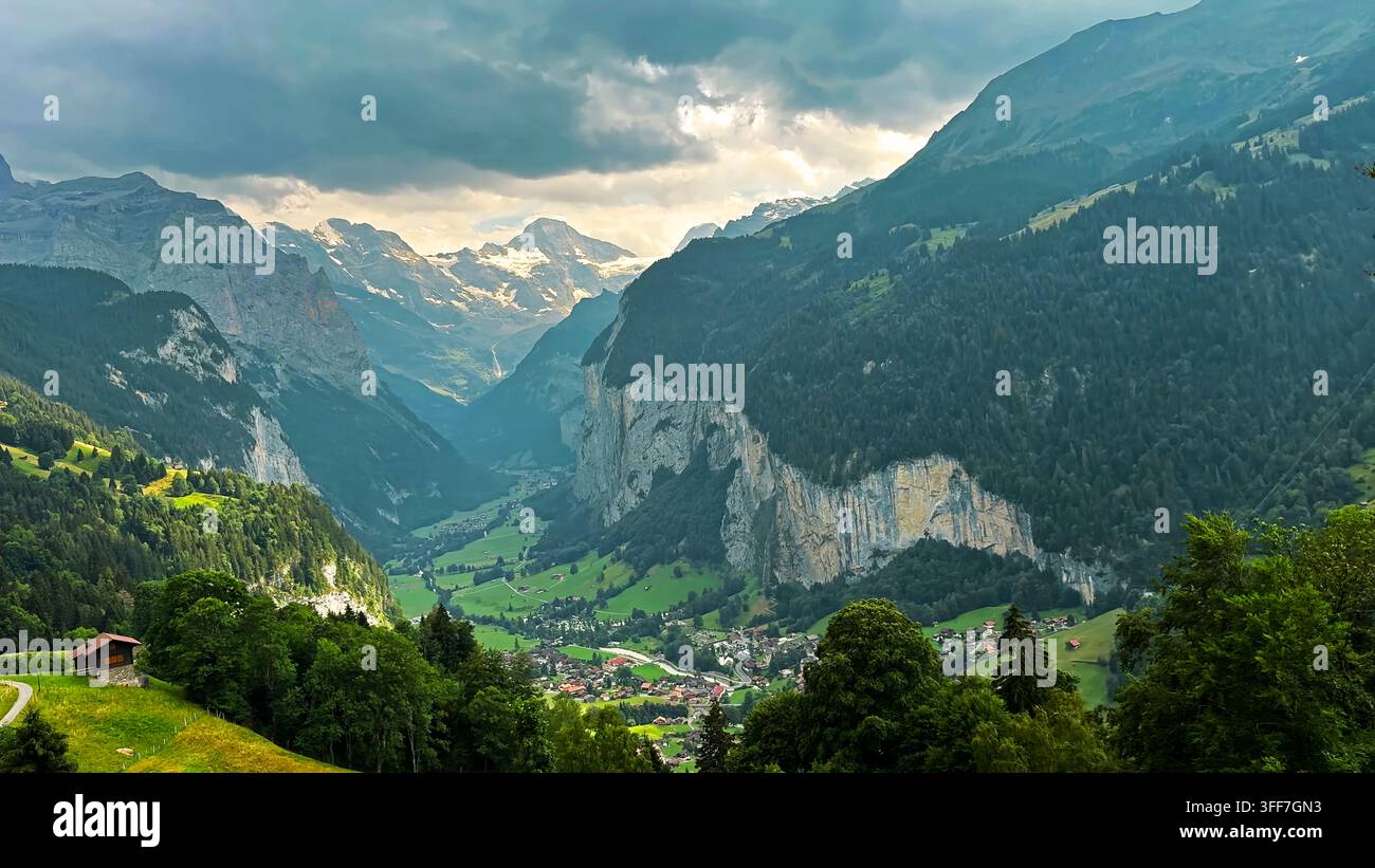 Valle di Lauterbrunnen sotto drammatiche montagne alpine. Vista panoramica della valle di Lauterbrunnen con prati verdi, villaggi alpini, scogliere boschive Foto Stock