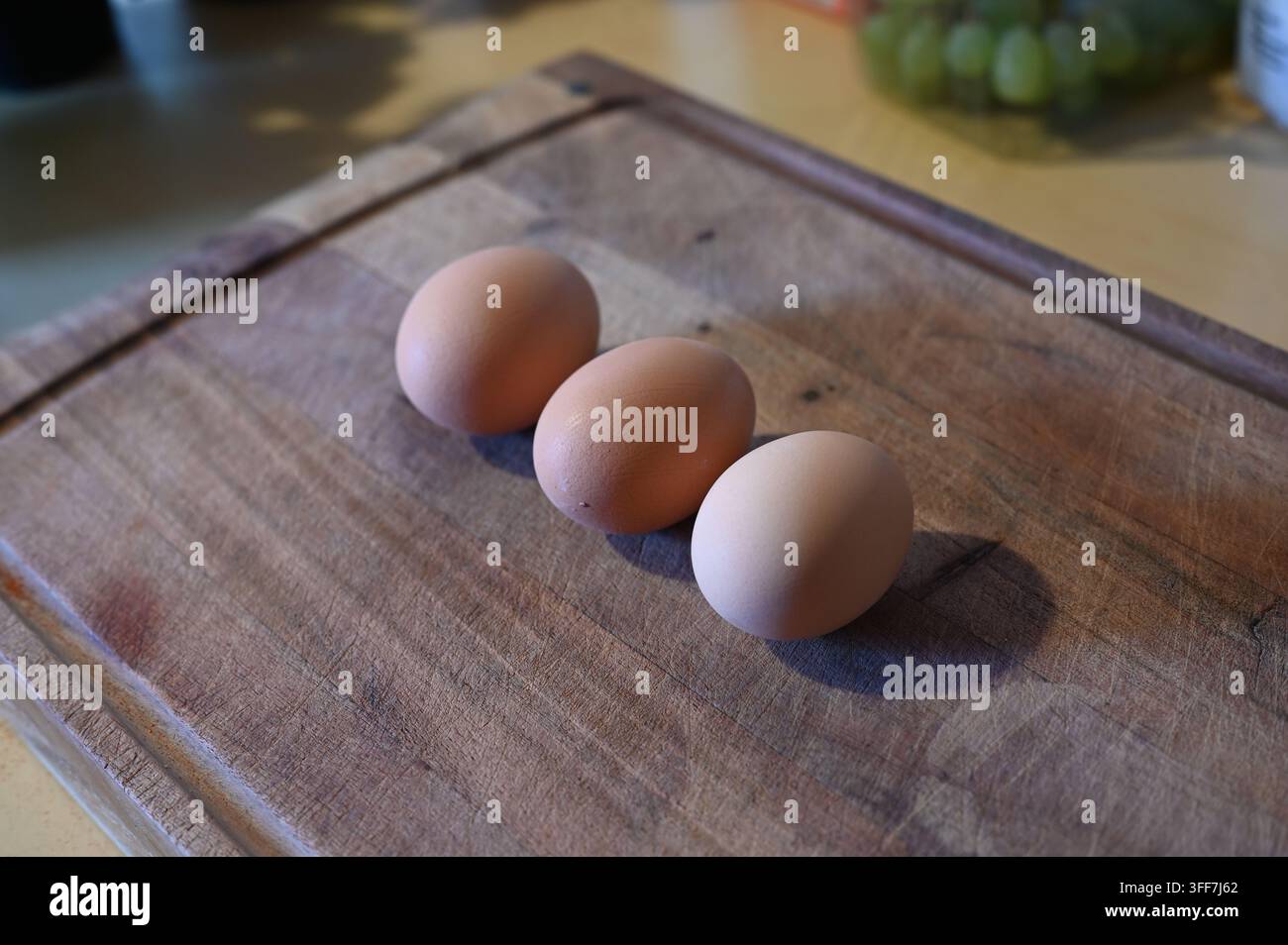 Tre uova di pollo marroni su un tagliere di legno rustico in una cucina. Foto Stock