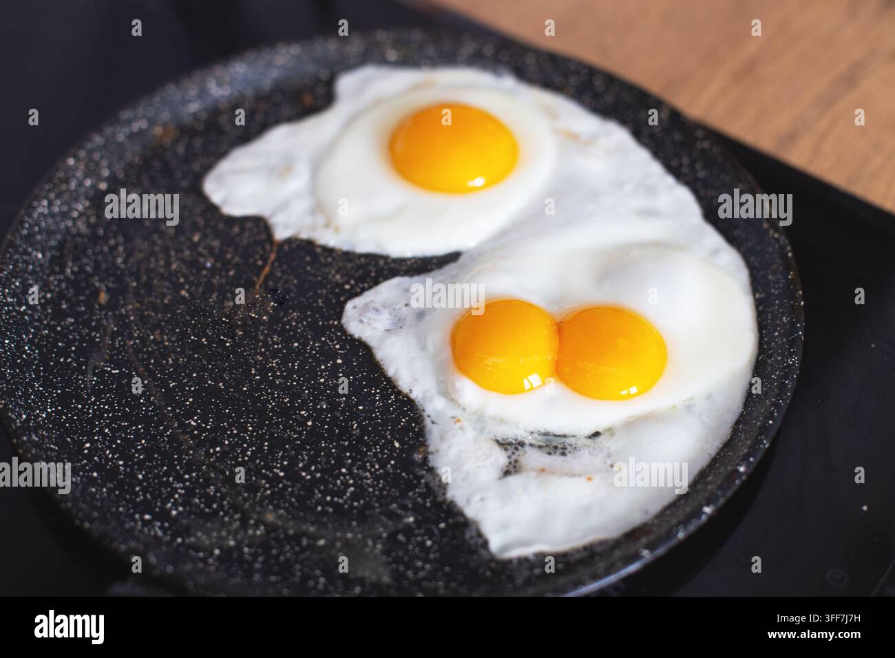 Friggere due uova, una con doppio tuorlo, in una padella antiaderente macchiata su un piano cottura a induzione Foto Stock