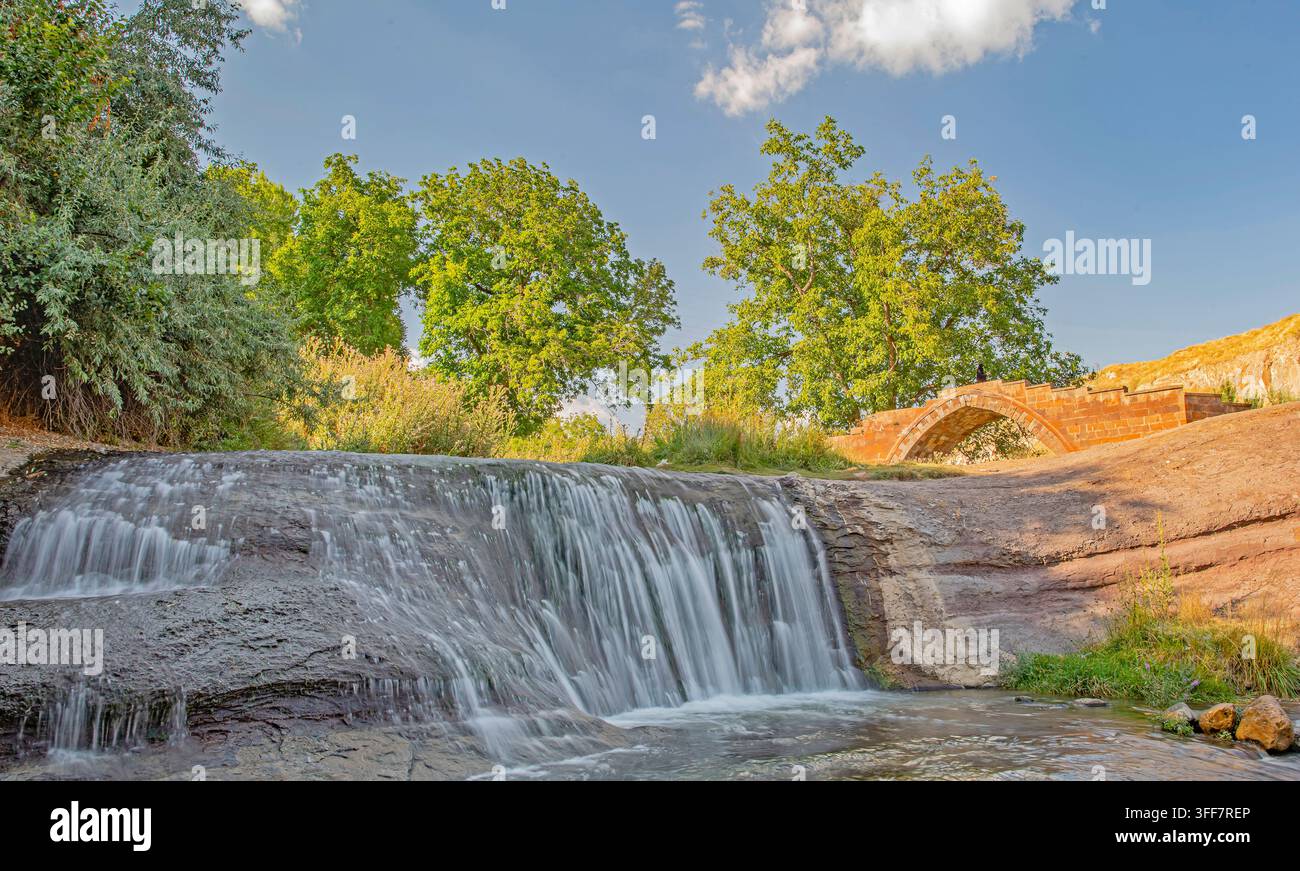 Il ponte storico di Bayindir situato nel distretto di Ahlat a Bitlis, Turchia, con una bellissima cascata naturale in primo piano. Un turista a Foto Stock