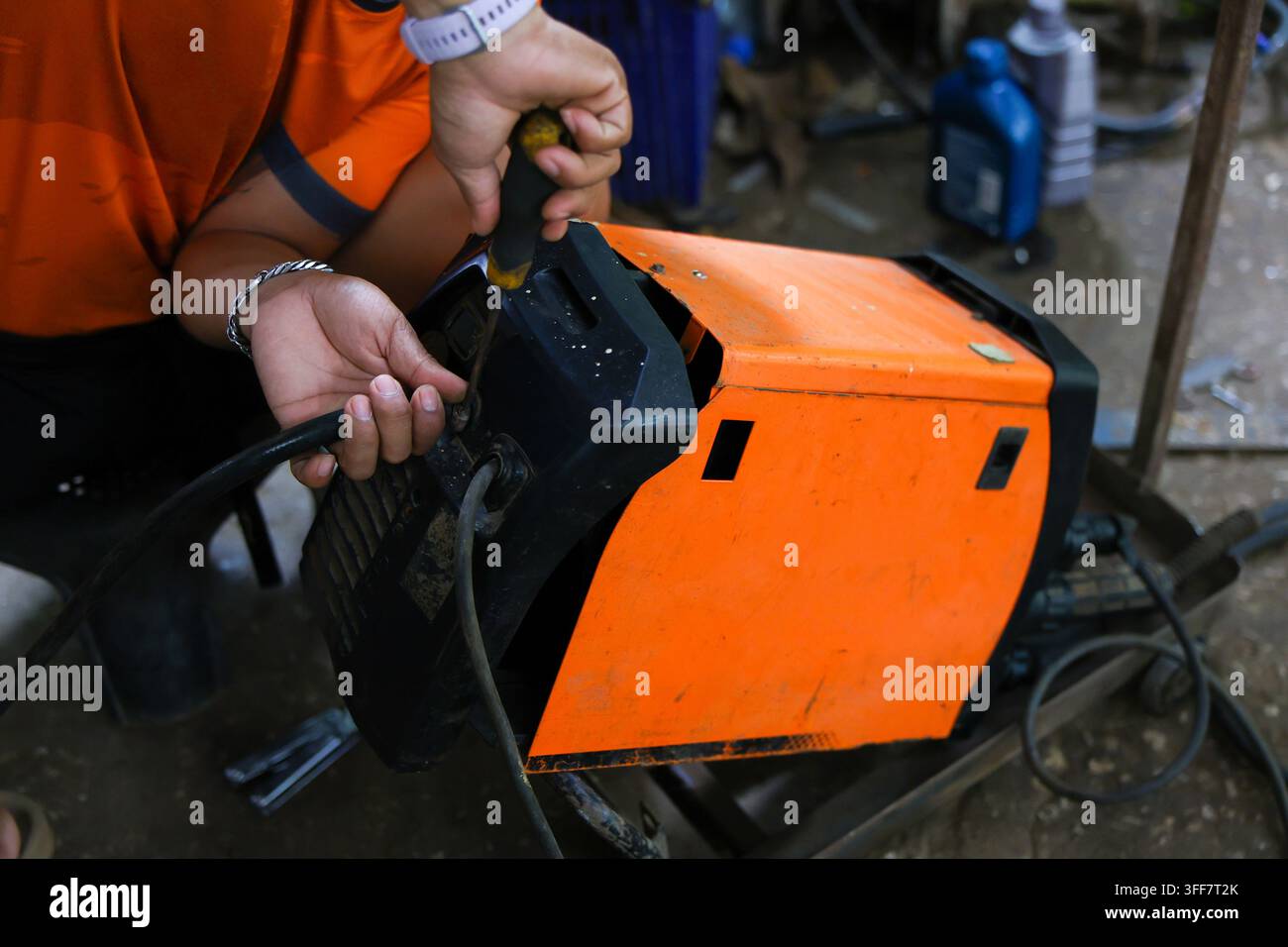 Un lavoratore con macchina saldatrice arancione, connessione cavo, officina industriale, attrezzatura utensili manuali, vista ravvicinata di un lavoratore che regola la connessione del cavo, saldatura arancione Foto Stock