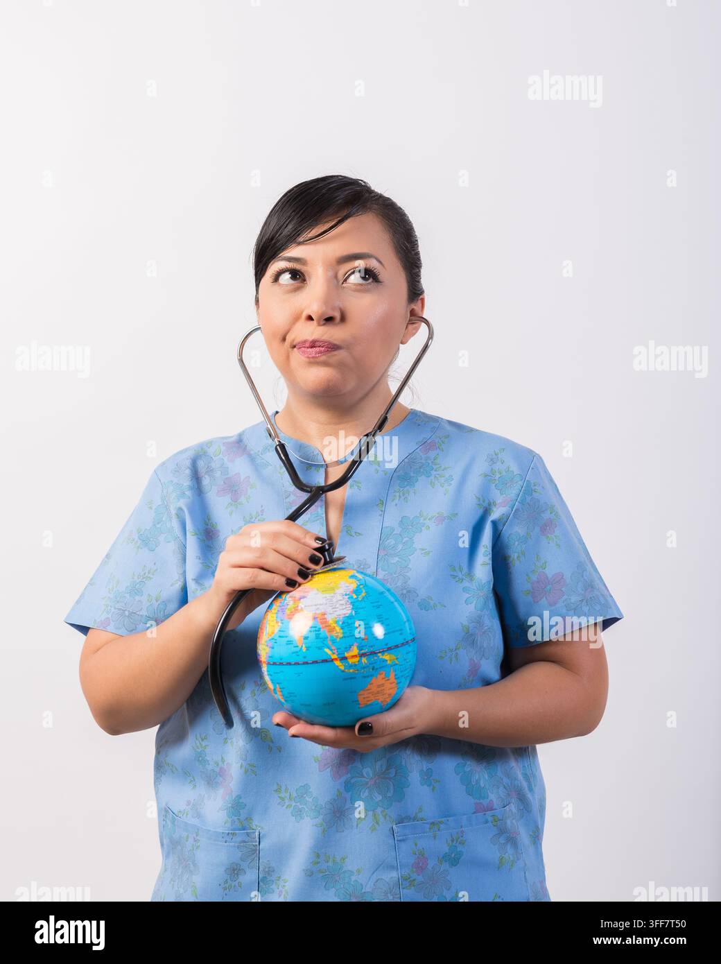Infermiera preoccupata esamina un globo con uno stetoscopio, simboleggiando la salute globale, i problemi ambientali e le preoccupazioni mondiali. Foto Stock