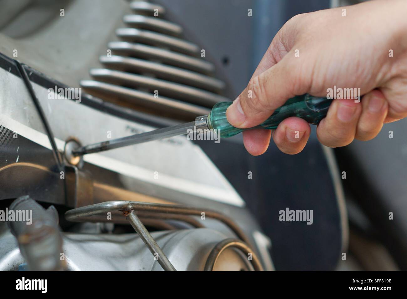 Prima vista di una mano che ripara un motore di classico motorino con un cacciavite verde, evidenziando la riparazione e la manutenzione meccanica fai-da-te. Foto Stock