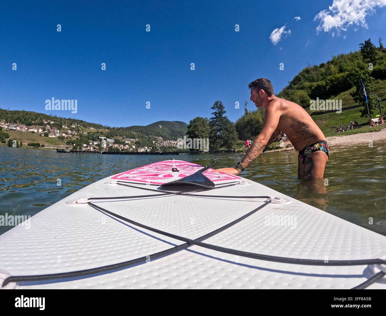 Un uomo si prepara per un'escursione in stand-up paddle nel Lago Serraia, Trentino, in una giornata di sole Foto Stock