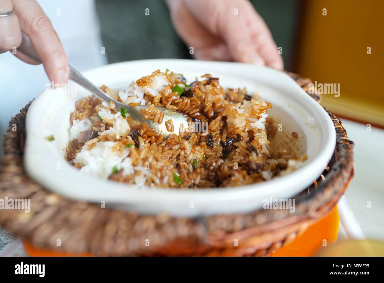 Una vista ravvicinata mostra riso bianco con salsa marrone e guarnizione verde mescolati in una ciotola bianca con un cucchiaio. Foto Stock