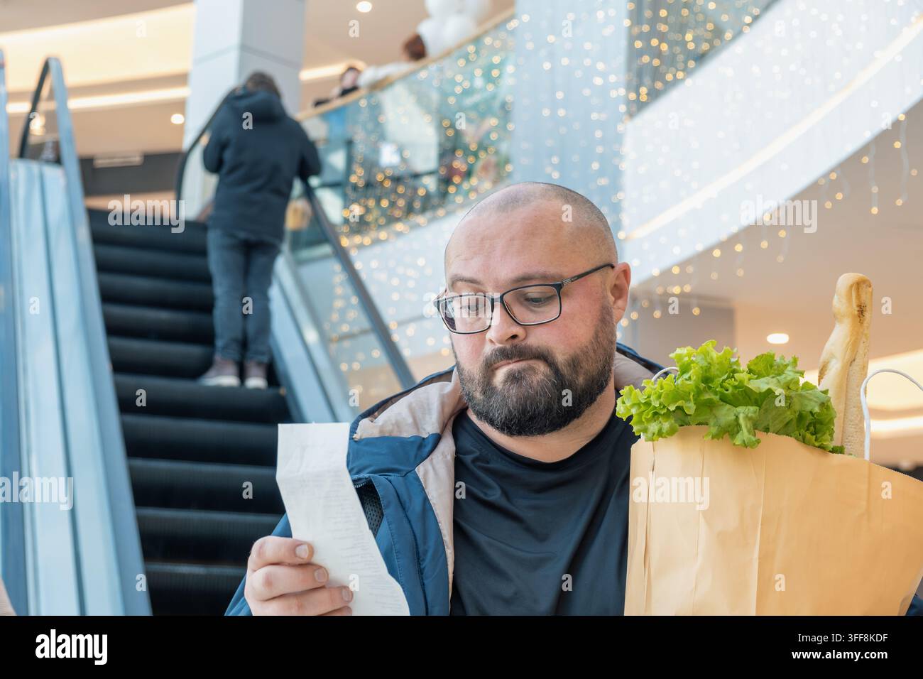 Uomo preoccupato con un sacco della spesa che controlla lo scontrino dopo lo shopping al supermercato. Aumento dei prezzi dei generi alimentari e una costosa fattura della spesa. Inflazione alimentare Foto Stock
