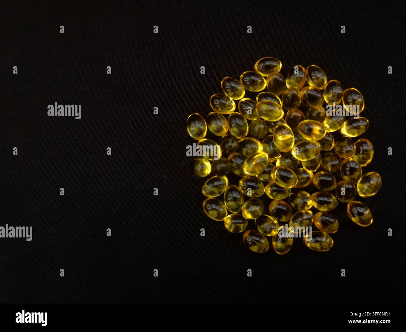 Una manciata di capsule trasparenti gialle su uno sfondo nero a forma di cerchio, spazio per il testo, vista dall'alto Foto Stock