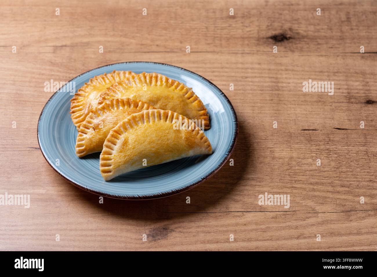 Empanadas dorate fatte in casa con bordi increspati, servite su un piatto blu sopra un tavolo di legno rustico. Foto Stock