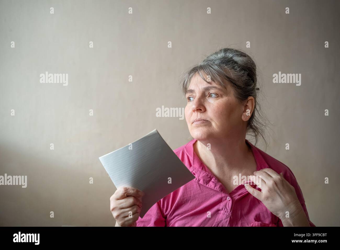 Donna matura che si rinfresca con un ventaglio di carta a casa. Consapevolezza della menopausa vampate di calore salute delle donne e benessere nella perimenopausa. Foto Stock