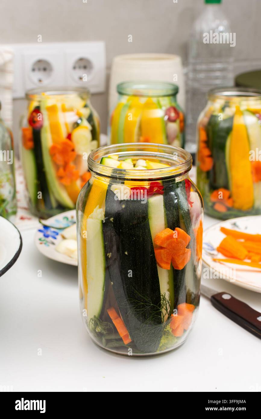 Le persone conservano le zucchine per l'inverno conservandole insieme ad altre verdure. I barattoli mostrano strati colorati di zucchine, carote e Sp Foto Stock
