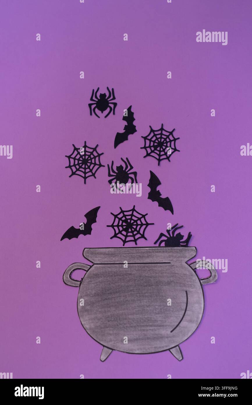 Composizione piatta di un allestimento di Halloween con un calderone ritagliato da carta da cui fuoriescono sagome nere di pipistrelli volanti, ragni rampicanti e ragnatele Foto Stock