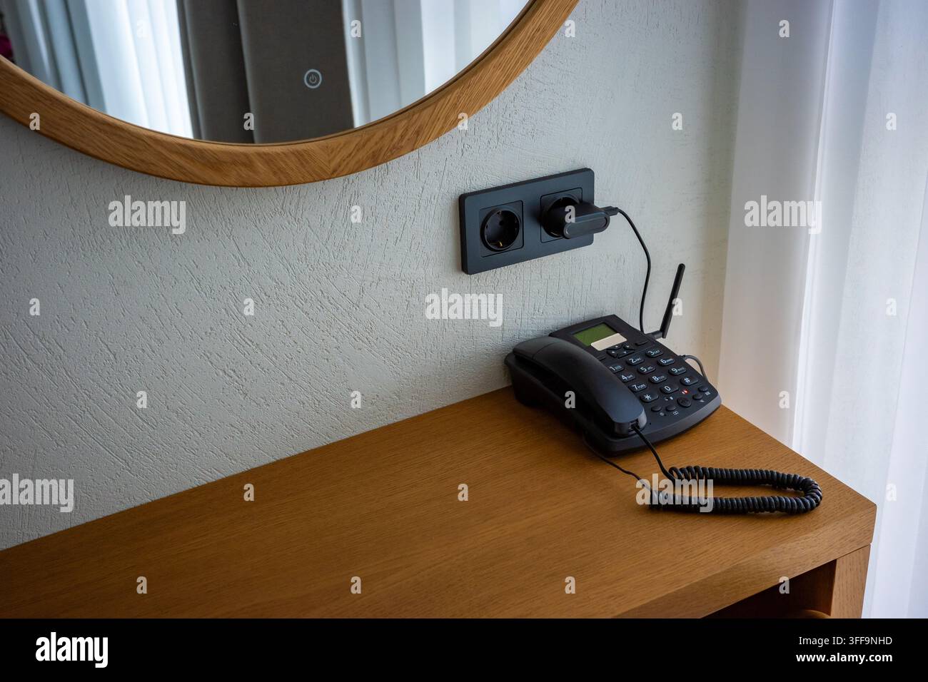 Telefono fisso nero su scrivania di legno accanto alla presa a muro, comunicazione tradizionale, servizio d'ufficio e alberghiero. Foto Stock