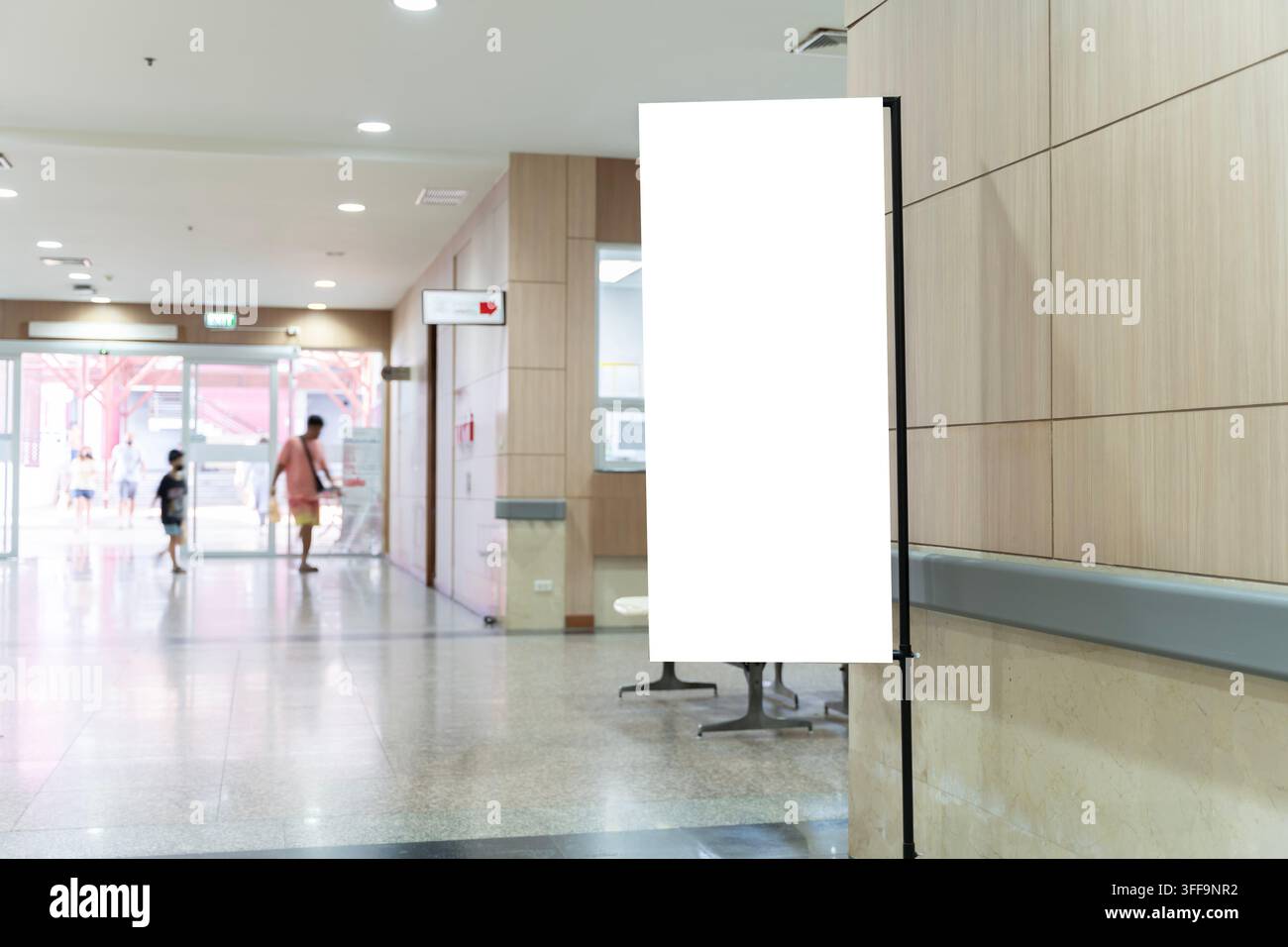 Corridoio luminoso con pavimenti lucidati e pareti rivestite in legno. Grande striscione bianco vuoto, pronto per il branding. Le persone passano, casuali e ignare. Foto Stock