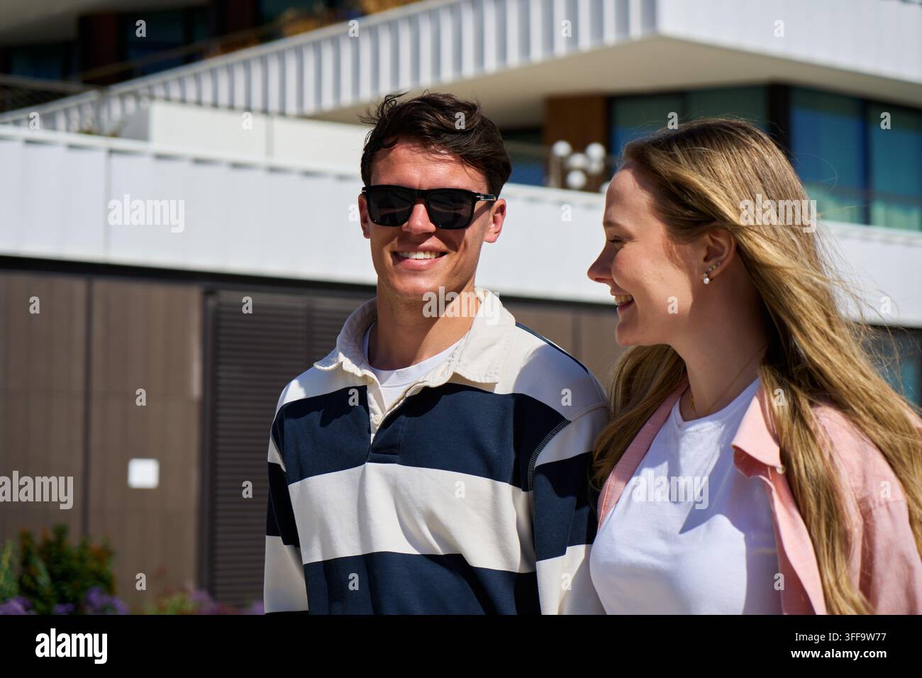 Giovane coppia sorridente che cammina insieme in una giornata soleggiata all'aperto. Foto Stock