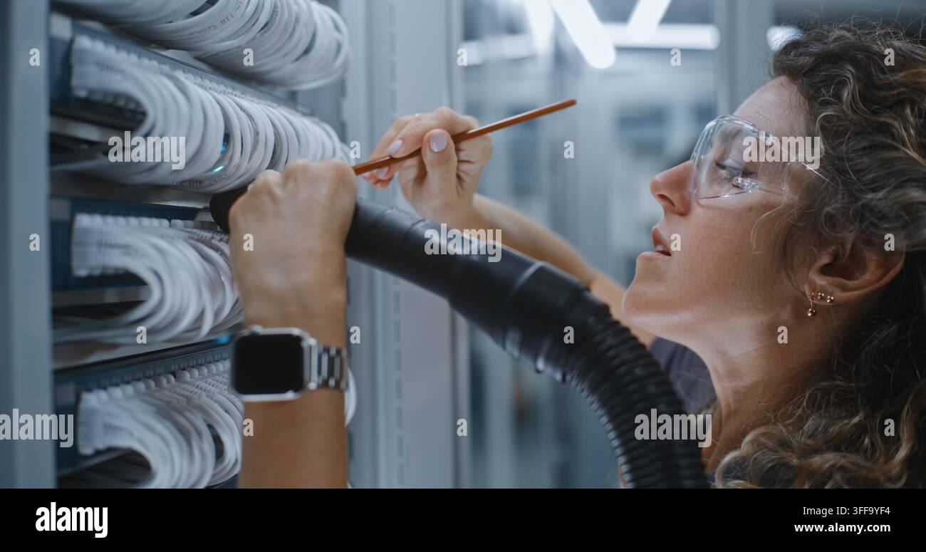 Pulizia specializzata delle strutture IT in azione. Professionista femminile rimuove l’accumulo di polvere dal cabinet del server. La sanità hardware di routine prolunga significativamente la durata dei server di dati aziendali. Foto Stock
