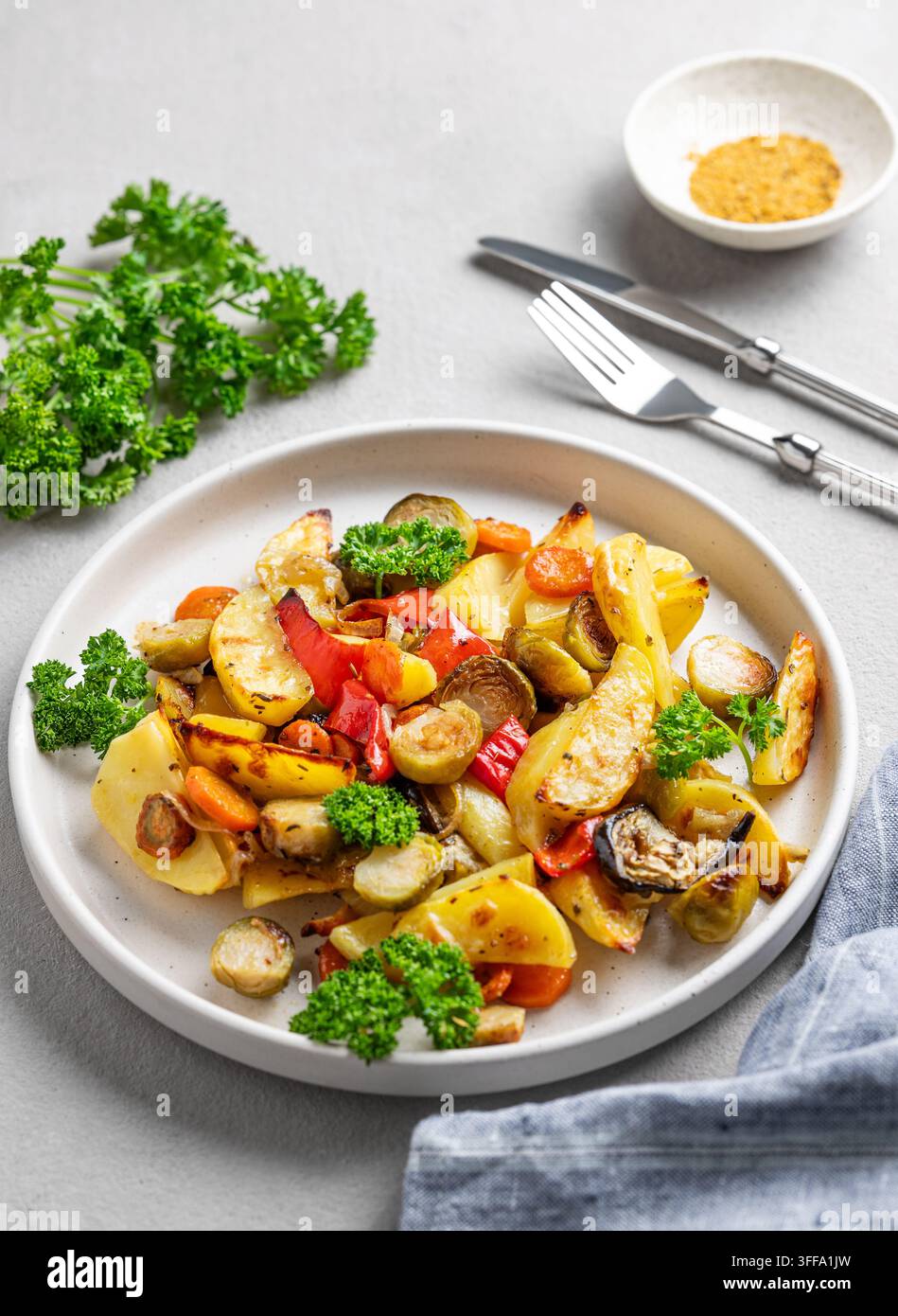 Verdure cotte al forno, patate, cavolo, peperone e cipolla su un piatto su uno sfondo chiaro con prezzemolo fresco. Concetto di piatto vegetariano. Foto Stock