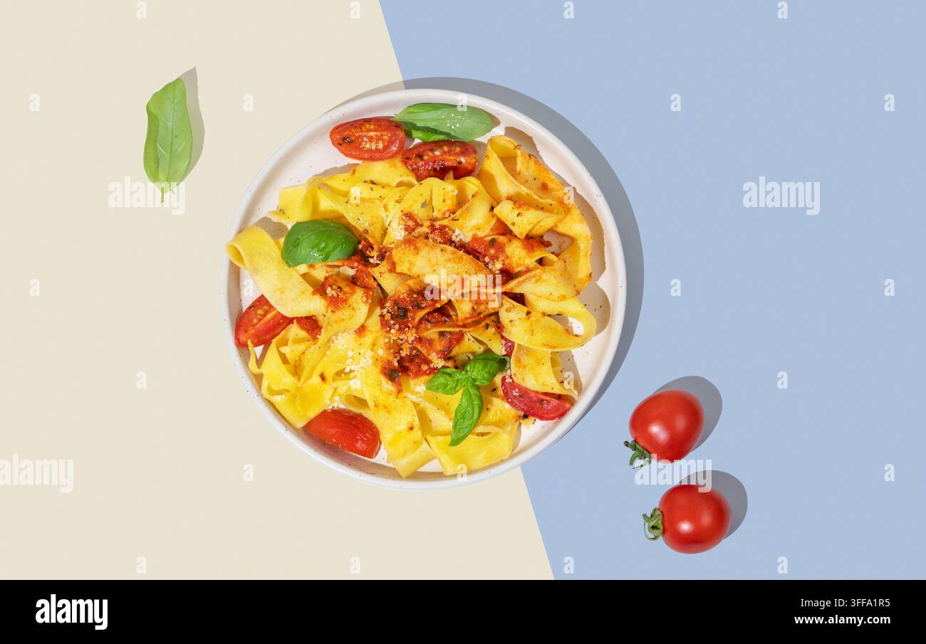 Tagliatelle o pappardelle con salsa di pomodoro, basilico e parmigiano su un piatto su uno sfondo giallo e blu con ombra. Concetto moderno o Foto Stock