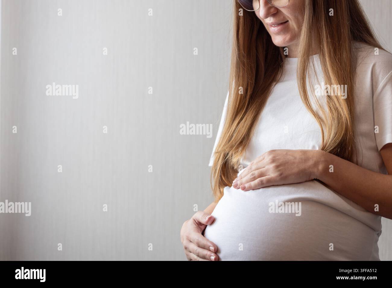 Donna incinta sorridente che tocca delicatamente il suo ventre. Foto Stock